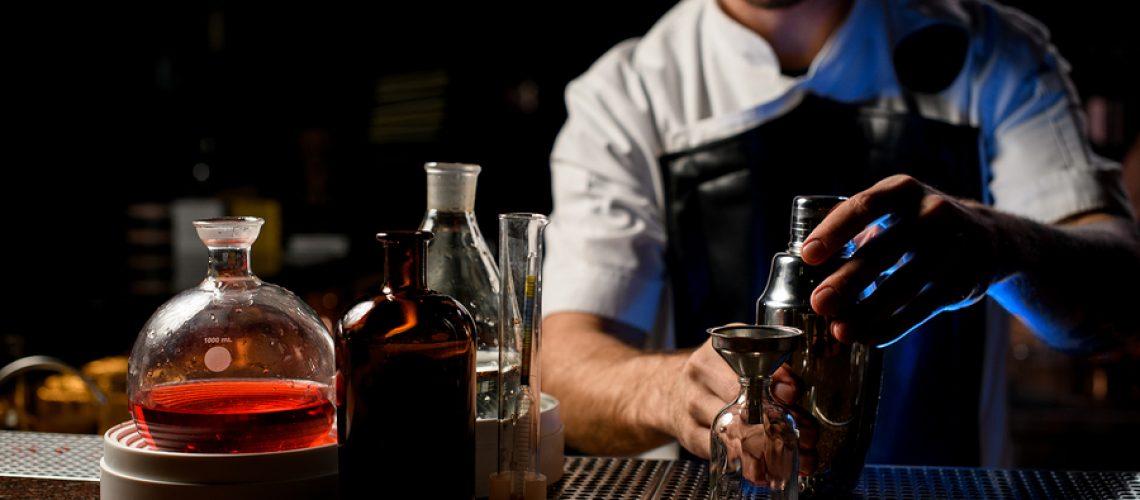 Professional male bartender holding in hands a steel shaker open it near the bartender equipment